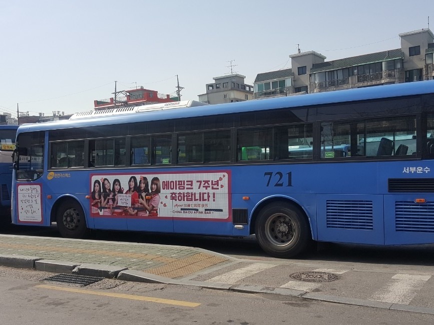 Apink 7th anniversary ad on the side of a blue Seoul city bus, with a photo of the group and a pink Korean headline