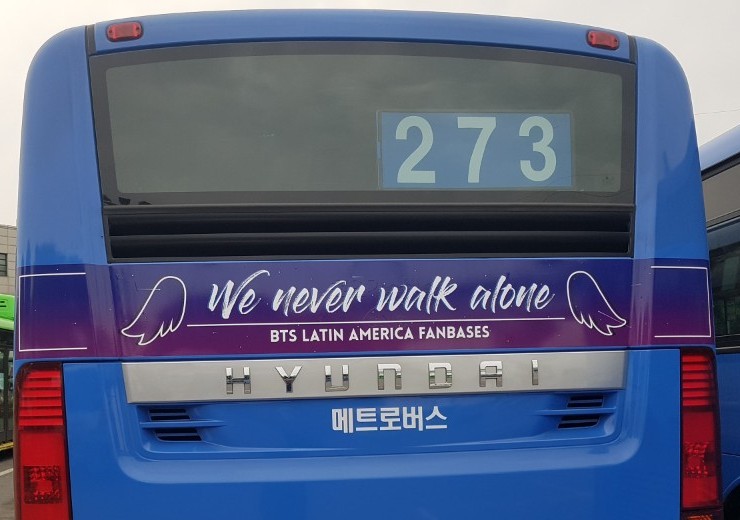 Rear of the bus with a purple strip reading "We never walk alone" and "BTS Latin America Fanbases" between two wing drawings