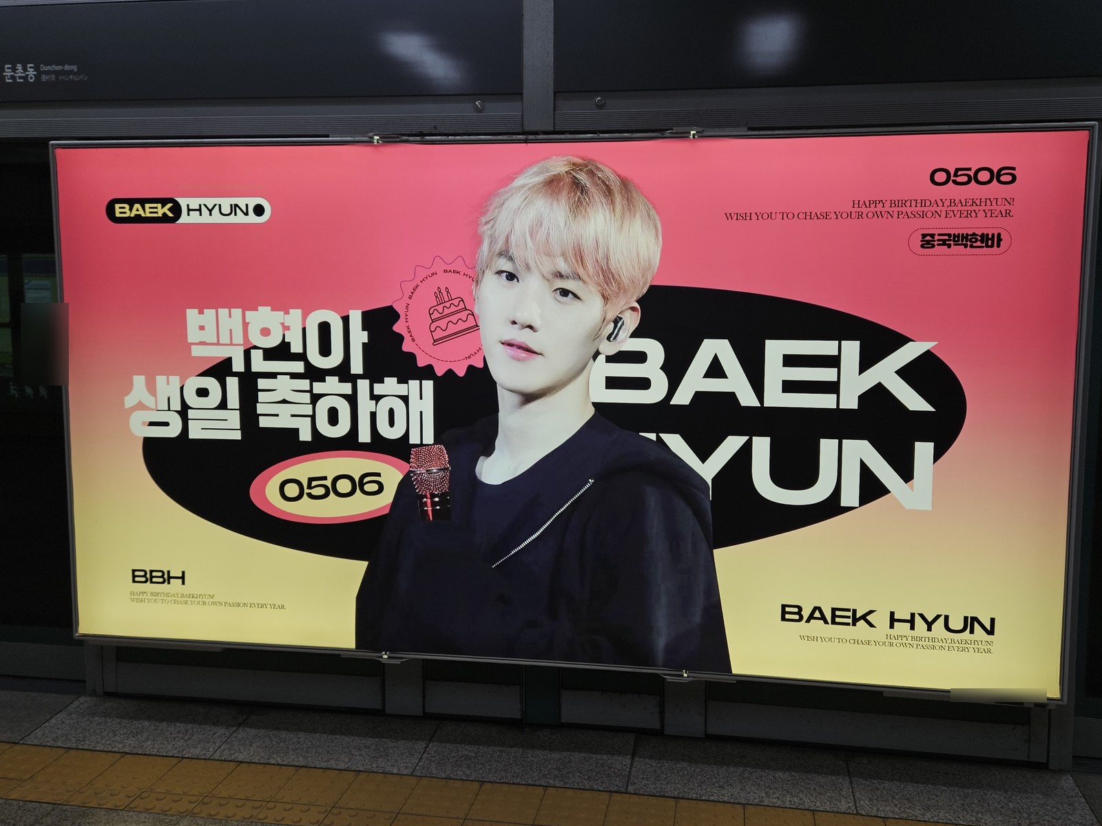 EXO Baekhyun birthday ad on a platform screen door at Olympic Park Station, a coral and yellow panel with his name in large letters