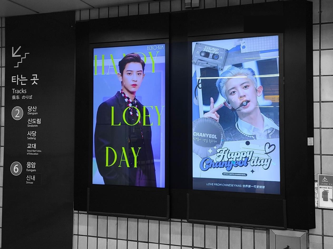 Two screens beside a transfer sign for Lines 2 and 6, one reading "HAPPY LOEY DAY" and one reading "Happy Chanyeol day"