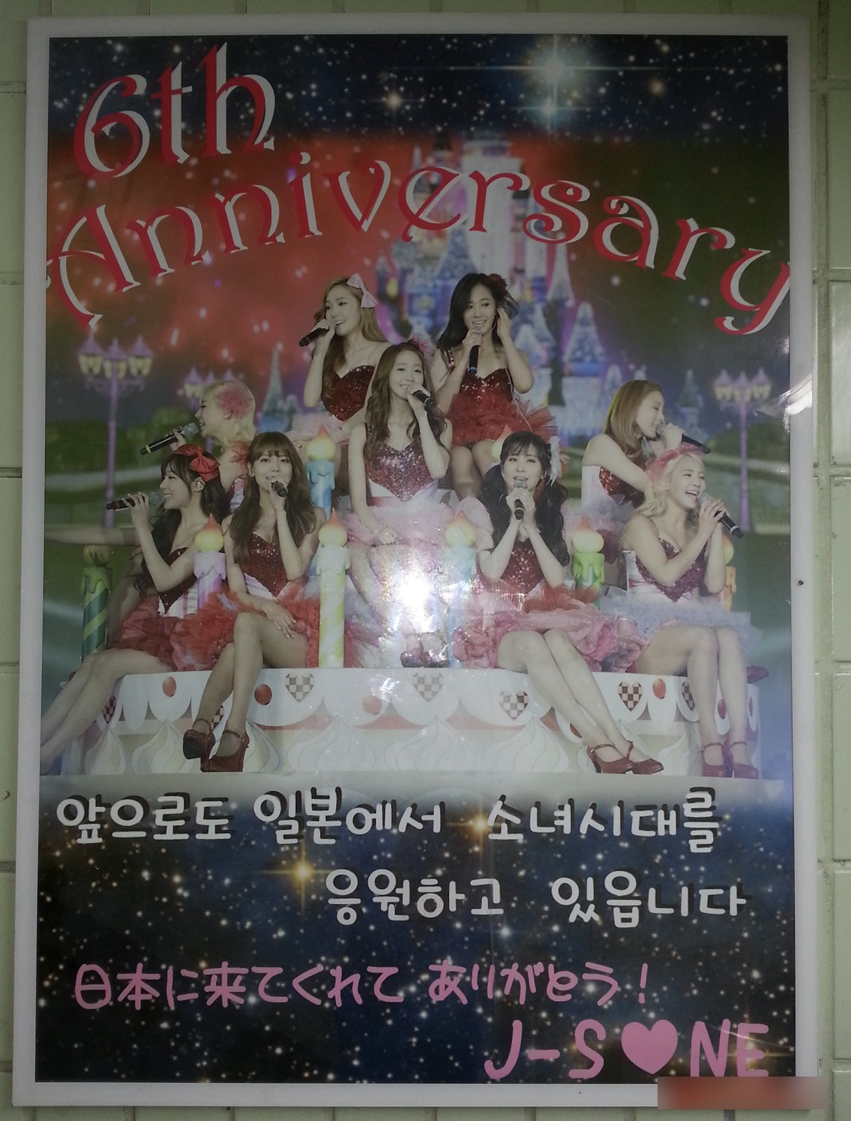 The same poster seen straight on, with "6th Anniversary" in red letters, a group photo and the signature J-S♥NE