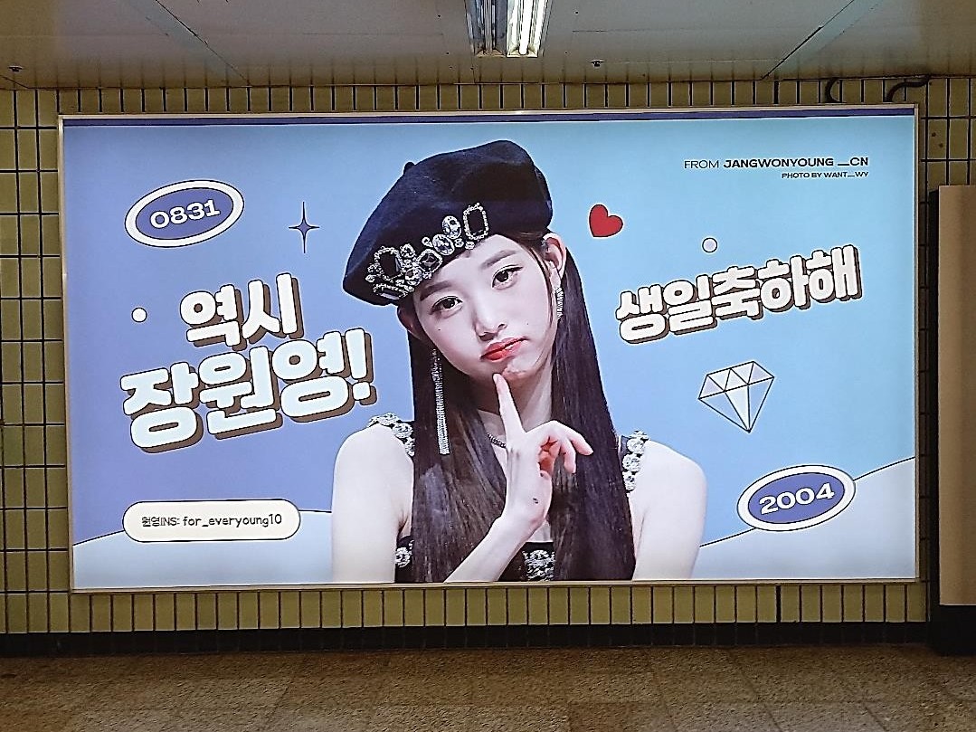 Jang Wonyoung birthday ad in a subway lightbox with a light blue background, a photo in a black beret and Korean birthday text in white bubble letters