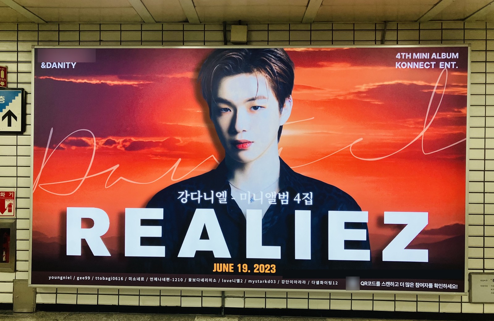 Kang Daniel comeback support ad on a wide lightbox at Sadang Station, with REALIEZ in large white letters over a red sunset sky