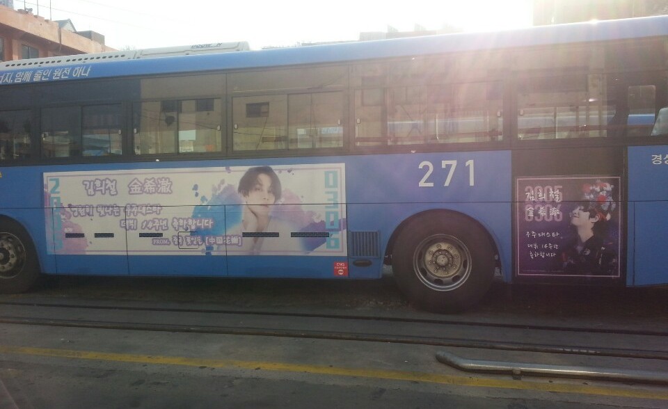 Road side of bus 271 in bright sunlight with a wide watercolour-style panel showing a portrait and Korean and Chinese lettering