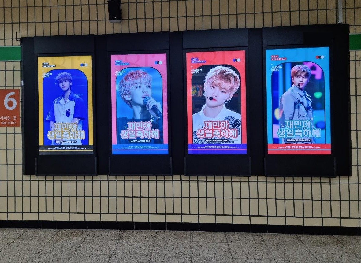 Jaemin birthday ad on four upright digital screens on a subway station wall, in yellow, pink, red and blue, each with a Korean birthday greeting