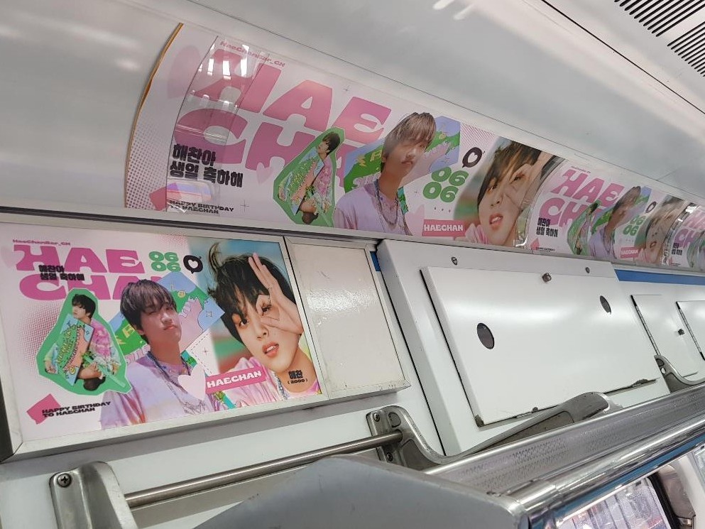 Haechan birthday ad inside a subway car, with a framed pink poster and a curved panel above it reading "HAECHAN" and a Korean birthday greeting