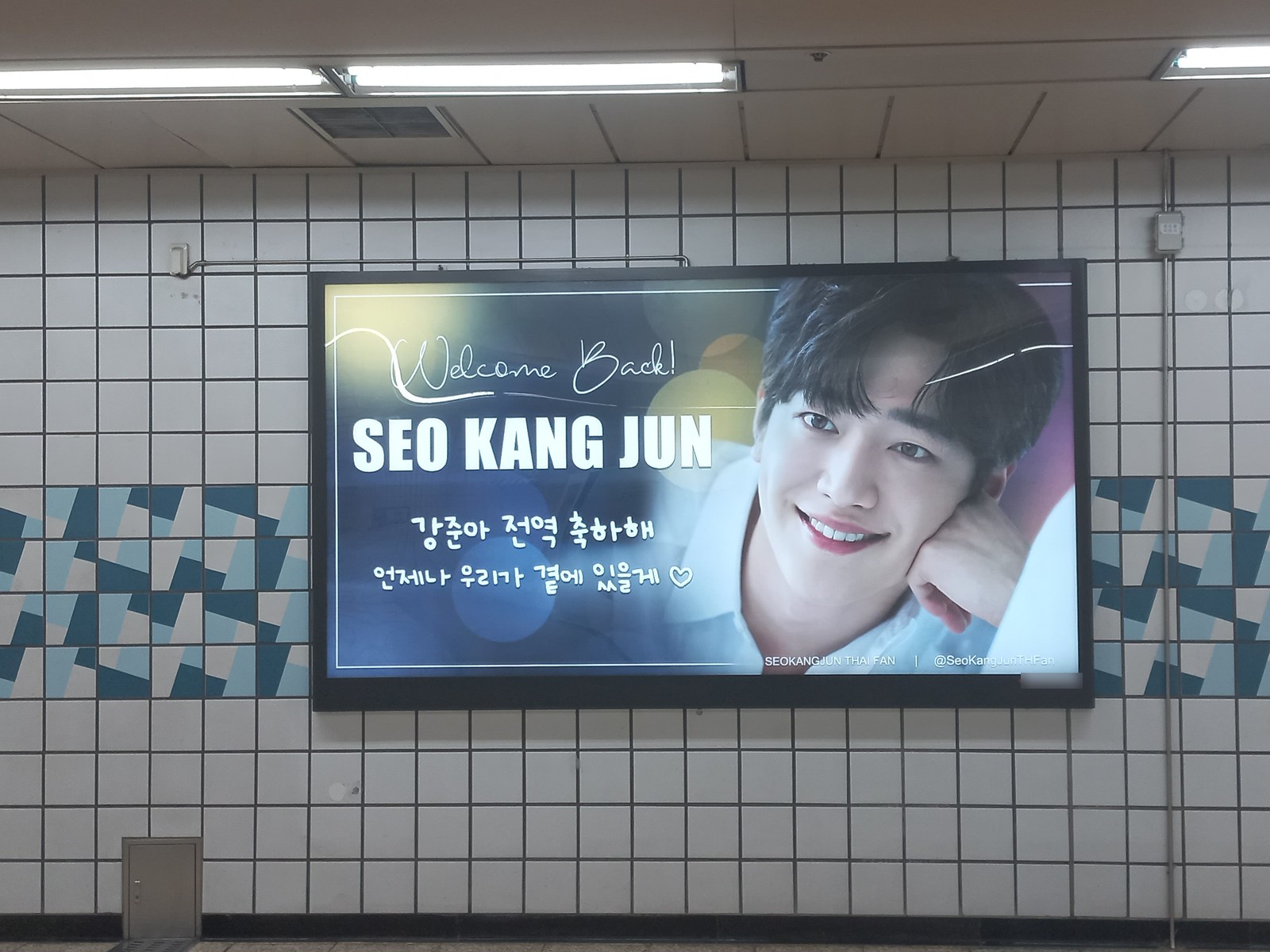 Wider view of the same lightbox on a white tiled wall at Hakdong Station, with Welcome Back! in script above the name